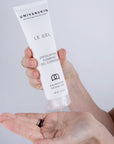 Hand holding a tube of Universkin Le Gel Exfoliating Foaming Gel Cleanser with a small amount on the palm.