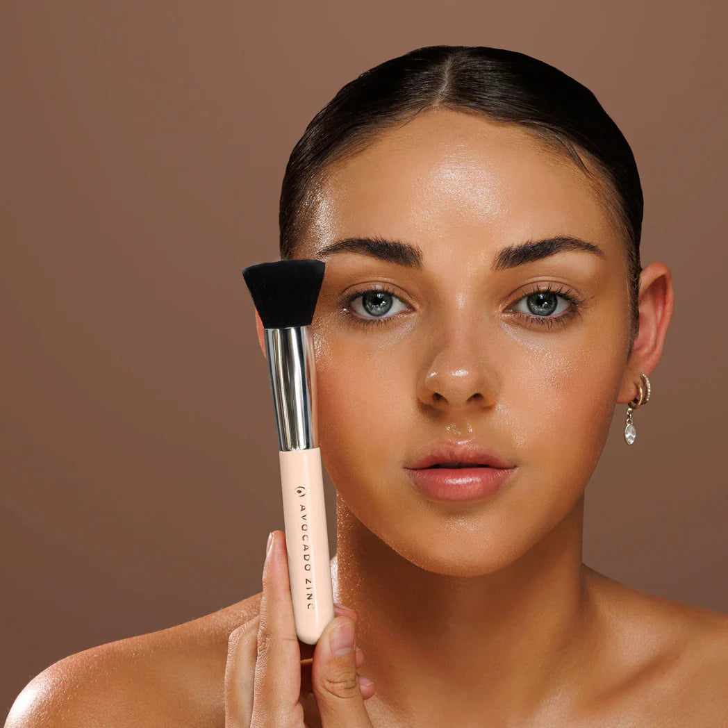 Woman holding an Avocado Zinc SPF Brush with black bristle head and beige handle