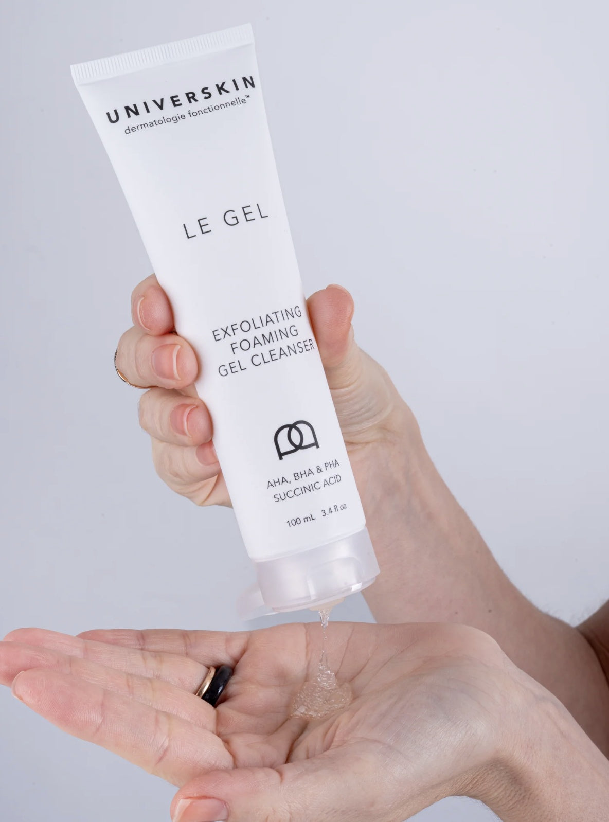 Hand holding a tube of Universkin Le Gel Exfoliating Foaming Gel Cleanser with a small amount on the palm.